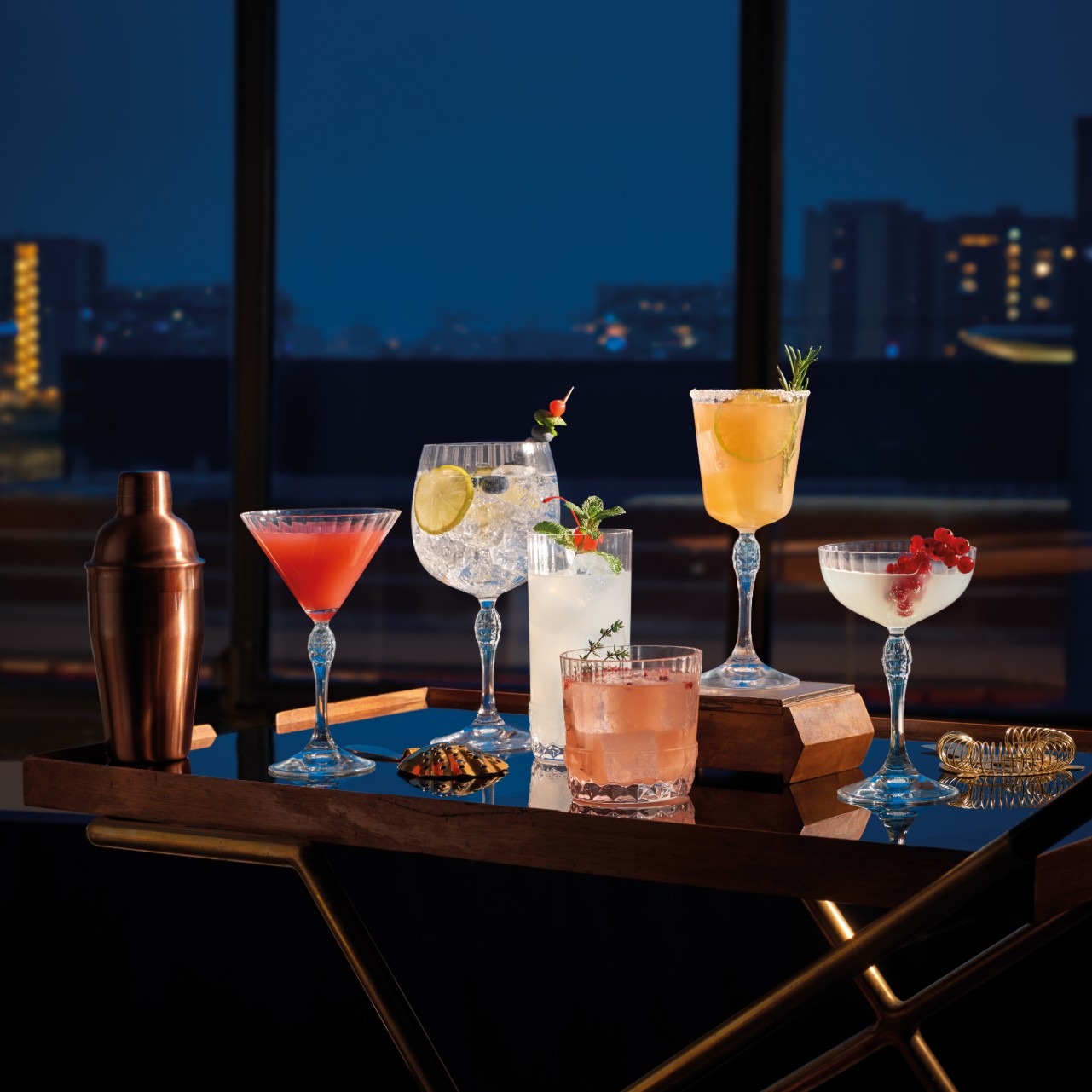 Speakeasy barware on a bar cart in a dark room, illuminated from the back
