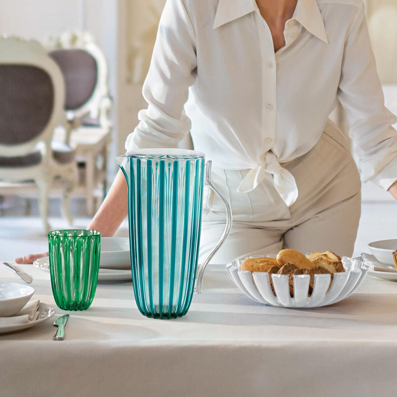 Guzzini Bellissimo emerald glass and turquoise pitcher with lid on a table beside a mother of pearl centerpiece