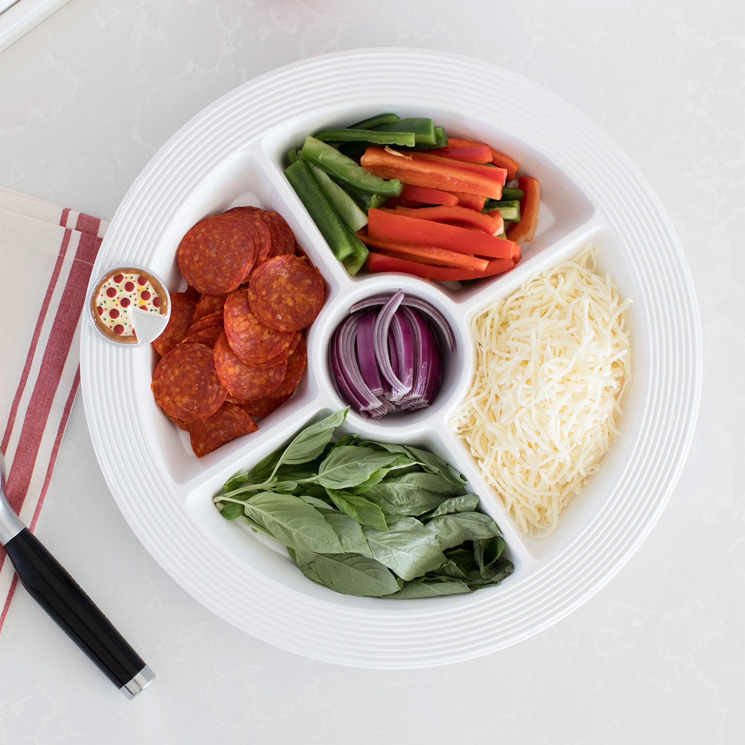 Nora Fleming mini Slice, Slice, Baby! shaped like a pizza with one slice missing, attached to a divided tray base filled with pizza toppings